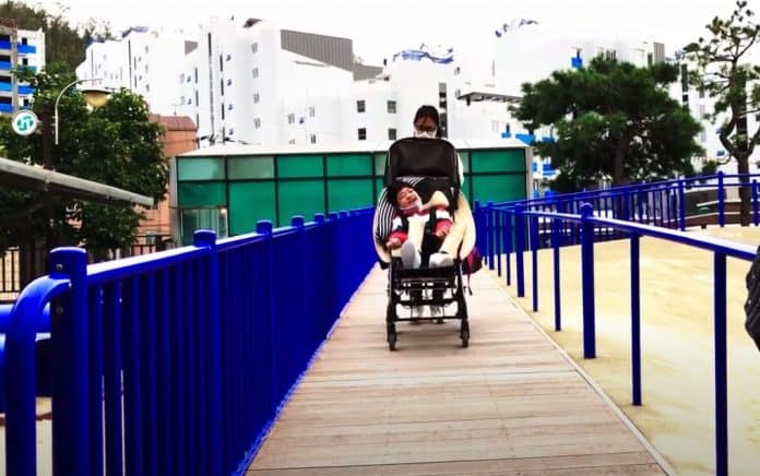 통합놀이터 홍박공원에서 미끄럼틀로 올라가는 경사로에서 휠체어에 앉은 아이를 밀어 주는 서경숙 강사
