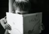 어린 아이가 두 손으로 책을 들고 읽다가 그 너머로 누군가를 응시하고 있다. ⓒunsplash