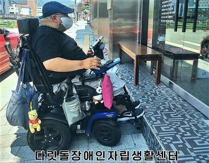 ▲전동휠체어 사용 장애인이 한 건물 입구 계단 앞에서 멈춘 채 안을 바라보고 있다. /사진=다릿돌장애인자립생활센터