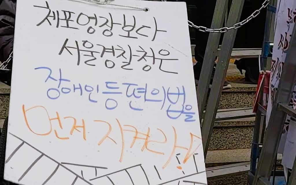 ▲피켓에 '체포영장보다 서울경찰청은 장애인등편의법을 먼저지켜라'는 문구가 적혀 있다. /사진=전장연 페이스북 라이브영상

