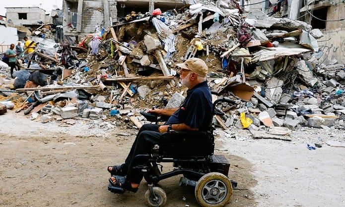 ▲2023년 10월 9일 가자지구 남부 라파에서 휠체어를 탄 팔레스타인인이 이스라엘의 공격으로 파괴된 건물 폐허 옆을 지나가고 있다. ⓒIbraheem Abu Mustafa/Reuters